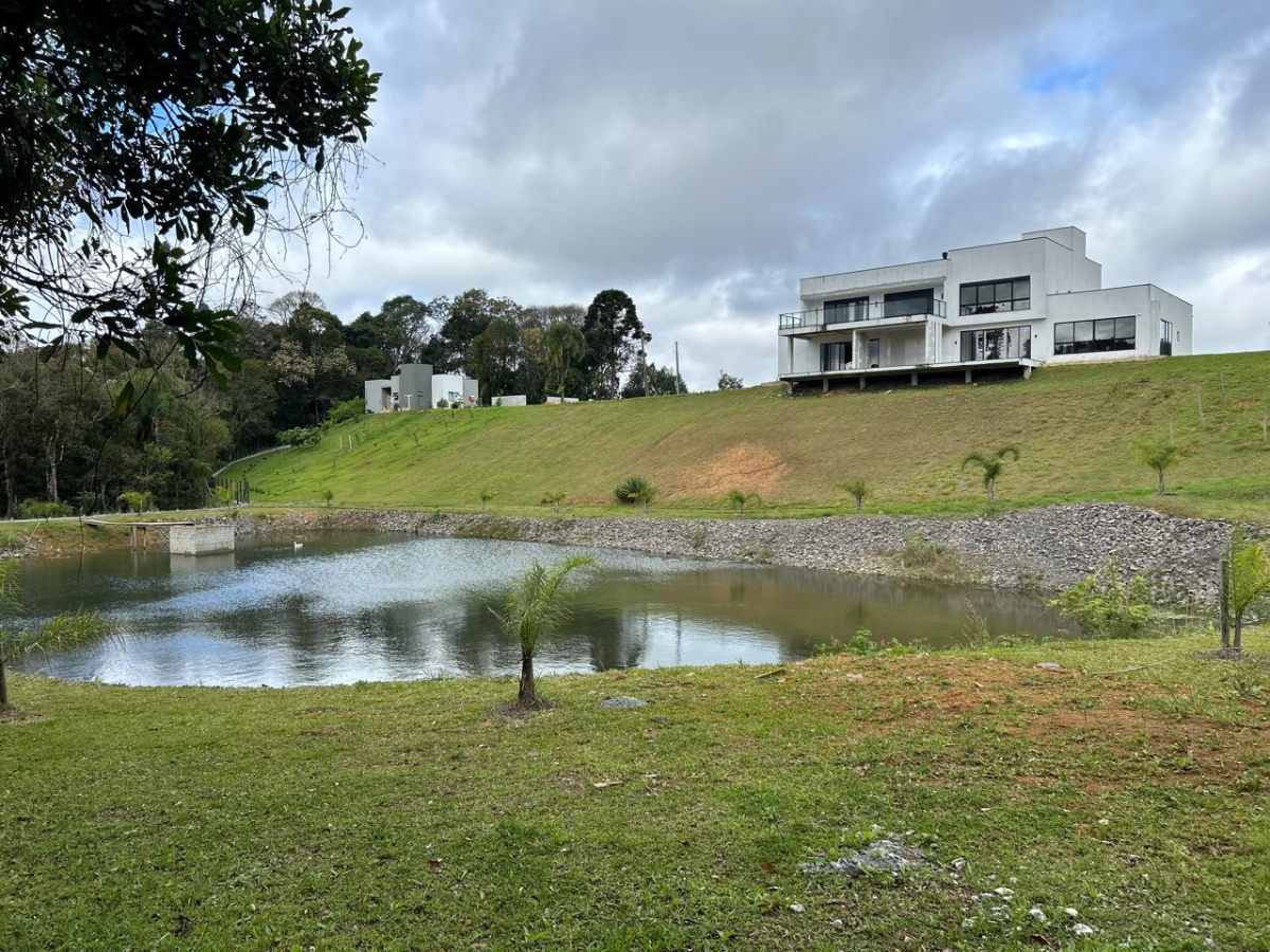 Casa contemporânea branca com terreno verde e lago em Campo Alegre
